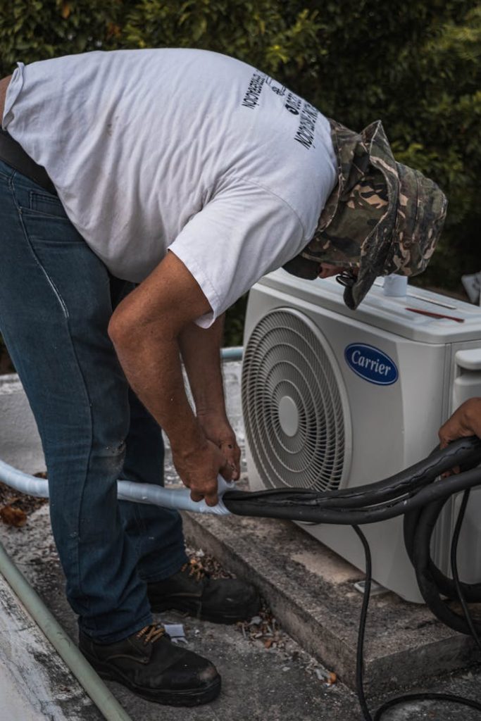 pexels-photo-5463576 A technician performs maintenance on an outdoor air conditioning unit, focusing on hose connections.